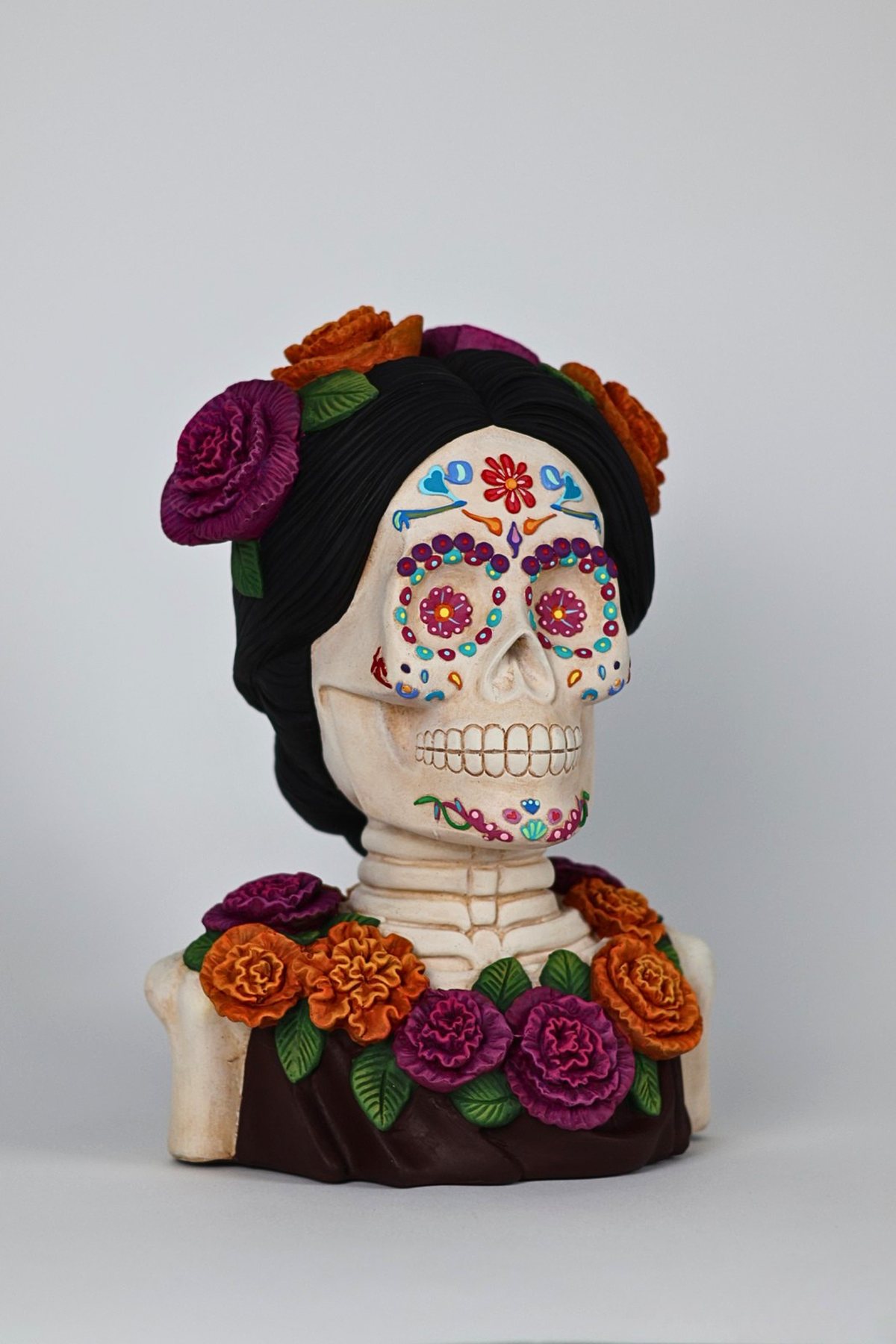 Catrina de cerámica pintada a mano con flores rojas y verdes sobre fondo oscuro